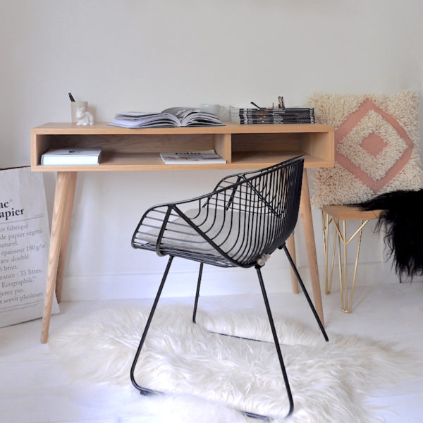 Mid century style black wire chair on a wool sheepskin rug at a desk.