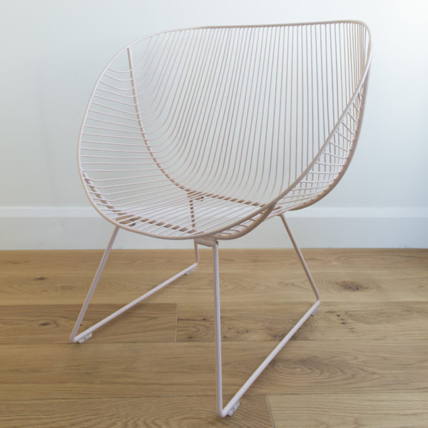 Blush pink outdoor wire chair with curved edges and wire legs.