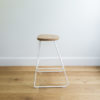 side view of kitchen stool with white wire legs & a hand sanded round oak seat
