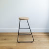 side view of kitchen stool with black wire legs & a rounded solid oak seat