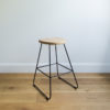 angle view of kitchen stool with black wire legs & a rounded solid oak seat
