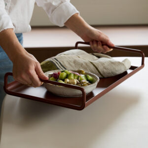 Ico Traders Metal All Day Tray in Chocolate red, being carried, while holding a bowl of salad