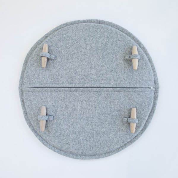 A grey, felted wool, round circle chair or stool pad / cushion, with zip running down the middle and wooden toggles.