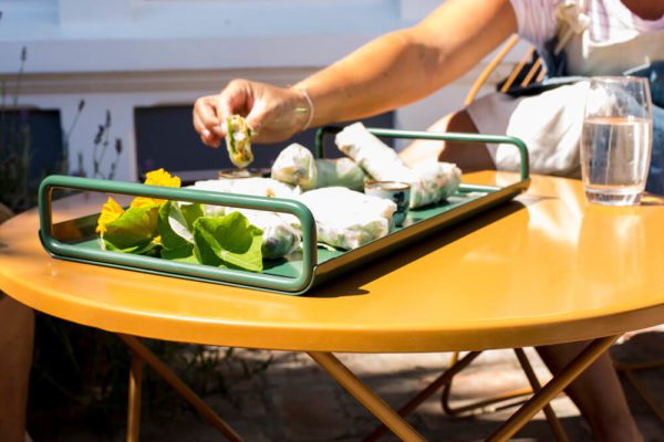 Curved metal tray holding fresh spring rolls on around outdoor metal table.