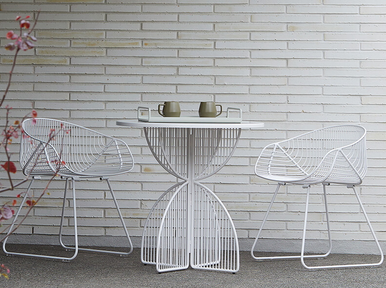 Outdoor wire dining setting by Ico Traders featuring two white wire chairs and a round wire table on a minimalist patio in New Zealand.